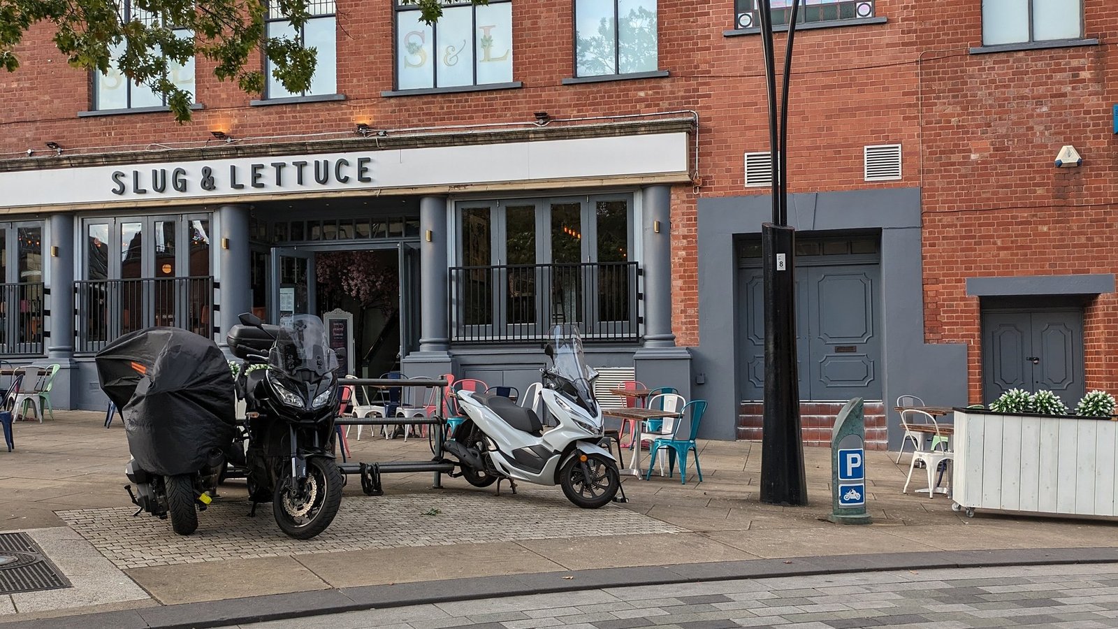 Motorcycles parked on a paved area beside a city street in Sheffield, with outdoor seating nearby